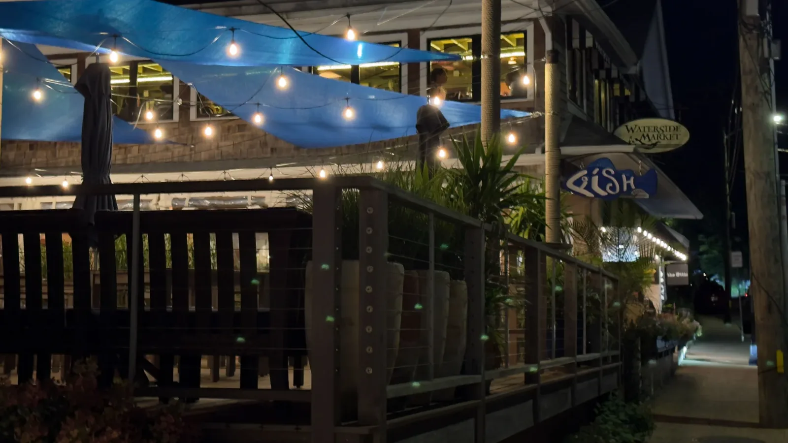 The deck at Fish MV at night, blue shade sails and string lights over the tables