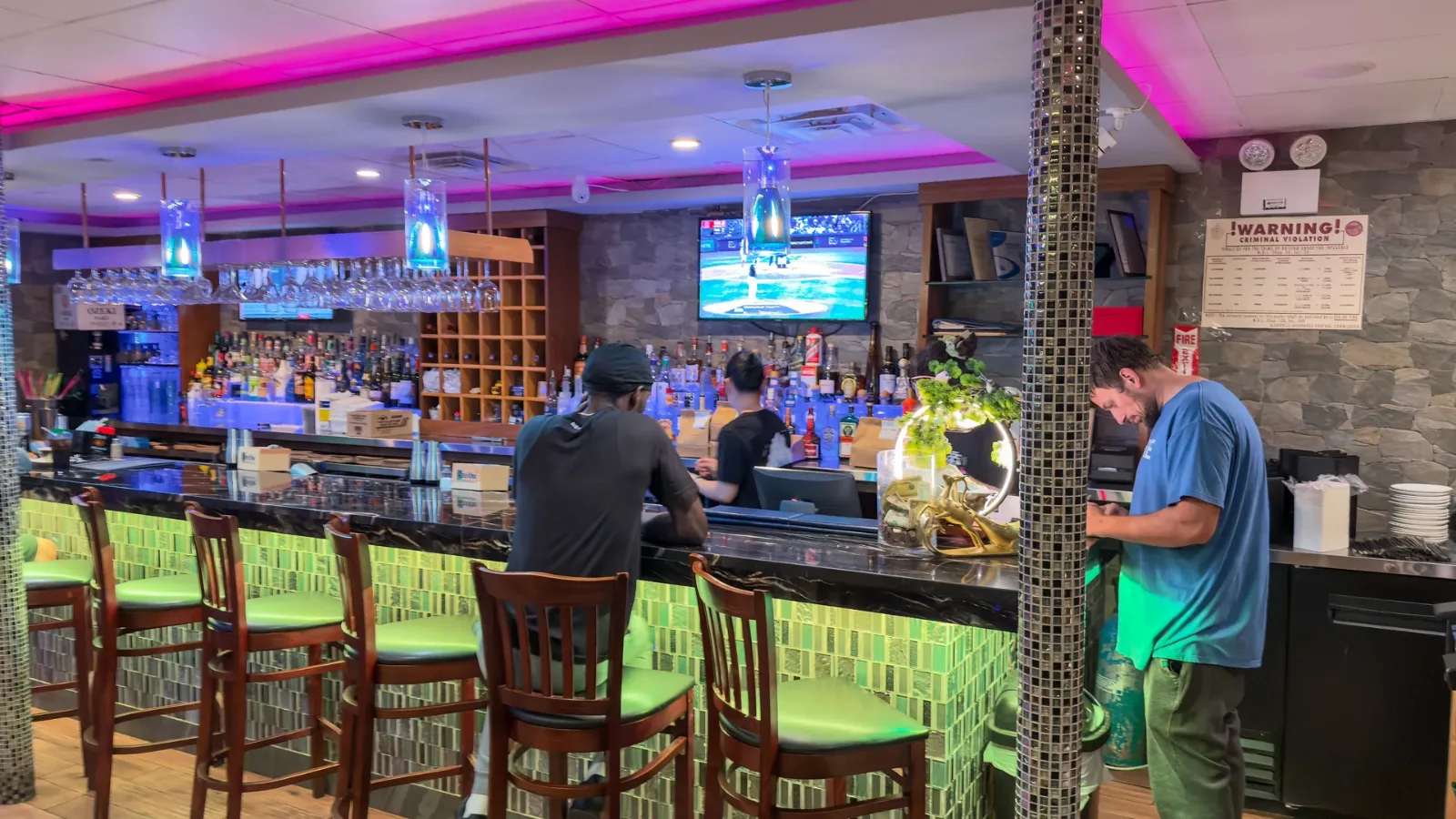 The bar at Mikado under pink and blue light, green tiled front and tall stools