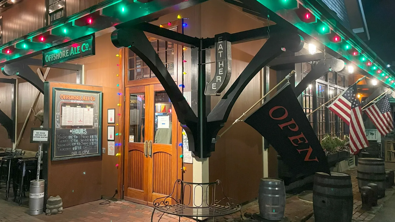 The side entrance at Offshore Ale under coloured lights in winter, open flag out and barrels by the door